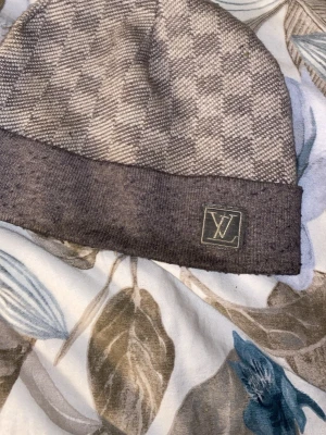 Grå mössa med rutmönster - Säljer en snygg grå mössa från med klassiskt rutmönster och logga framtill. Mössan har en bred uppvikt kant och är tillverkad i mjukt stickat material som känns lyxigt och bekvämt. Perfekt accessoar för att höja din outfit.