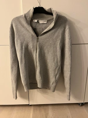 Grå ziptröja från selected home - Snygg grå stickad ziptröja selected home med hög krage och hel dragkedja framtill. Tröjan har ribbade muddar vid ärmslut och nederkant, perfekt för lager-på-lager. Enkel och stilren design som passar till det mesta. Storlek S men skulle säga att den sitter mer som M. Tröjan är aldrig använd och prislappen sitter kvar! Nypris 800 mitt pris 500