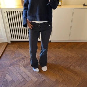 Mörkgrå cargobyxor med fickor - Säljer ett par mörkgrå cargobyxor med raka ben och flera praktiska fickor på sidorna. Byxorna har knapp- och dragkedjestängning samt detaljer i metall. Perfekta för en avslappnad och trendig stil.