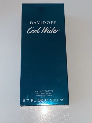 Davidoff Cool Water Eau de Toilette - Davidoff Cool Water Eau de Toilette i en snygg blå rektangulär kartong. Flaskan innehåller 200 ml och har en fräsch, klassisk doft. Förpackningen har en modern och stilren design med vit text på framsidan.