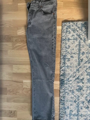 Grå Levi's raka jeans - Säljer ett par grå jeans från Levi's med klassisk femficksmodell och raka ben. Jeansen har en läderpatch bak i midjan och den ikoniska röda Levi's-lappen på bakfickan. Tillverkade i slitstark denim, perfekta för en avslappnad stil.
