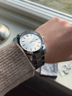 Silverfärgad klocka från Parnis - Stilren klocka från denuase med silverfärgad länk i metall och vit urtavla. Klockan har romerska siffror, datumvisning och klassisk design. Perfekt accessoar för dig som gillar en clean och tidlös look.