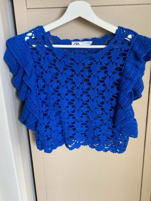 Blå virkad topp från Zara - Snygg blå virkad topp från Zara med korta volangärmar och ett genombrutet blommigt mönster. Toppen har en boxig passform och är gjord i mjukt garn, perfekt för lager på lager eller som statement-plagg.