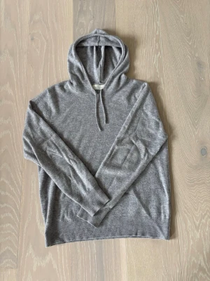 Grå cashmere hoodie från Sayless - Mjuk och stilren grå hoodie från Sayles i lyxig cashmereblandning. Klassisk modell med huva och dragsko, ribbade muddar vid ärmslut och nederkant. Perfekt för dig som gillar en clean och avslappnad look. Vid intresse är det bara att höra av sig. Pris går att diskutera 