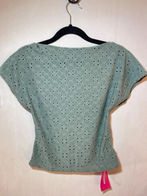 Grön broderad blus med öppen rygg - Snygg ljusgrön blus med broderade detaljer och hålmönster i hela tyget. Blusen har korta ärmar och en avslappnad passform, perfekt för varma dagar. Tillverkad i mjuk bomull som känns skön mot huden. Helt ny med prislapp. Shein, storlek L. Djur, rök och parfymfritt hem.