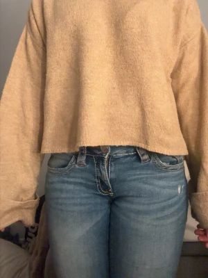 Beige croppad stickad tröja - Mysig beige stickad tröja med croppad passform och långa, vida ärmar. Tröjan har en enkel design utan synliga detaljer eller mönster.  