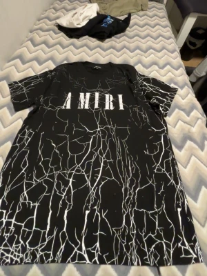 Svart Amiri t-shirt med vit marmorprint - Säljer en svart t-shirt från Amiri i storlek M med vit marmorliknande print över hela tröjan och stor vit AMIRI-logga på bröstet. Klassisk rund hals och korta ärmar. Perfekt för dig som gillar streetwear och vill sticka ut.