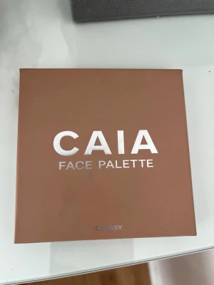 CAIA Face Palette Classy - Snygg face palette från CAIA i färgen Classy. Paletten innehåller contour, bronzer, blush och highlight i varma, naturliga toner. Kommer i en stilren, beige/brun fyrkantig förpackning med spegel. Perfekt för att skapa en fräsch bas och glow.