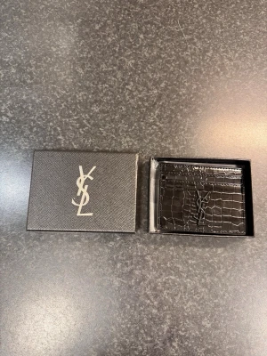 Svart kortfodral i krokopräglat läder - Snyggt svart kortfodral  i krokopräglat läder. Fodralet har flera kortfack och den  i metall på framsidan. Perfekt för dig som vill ha en stilren och lyxig accessoar i fickan.