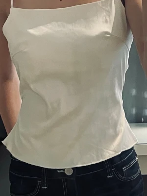 Gräddvit topp med öppen rygg och knyt - Säljer en stilren gräddvit linnetopp med tunna axelband och öppen rygg med knyt. Jättefint skick, inga defekter alls. 🤎