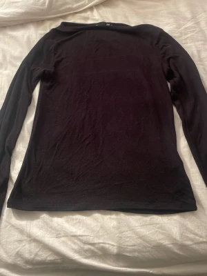 Svart långärmad topp - En enkel och stilren svart långärmad topp i mjukt material. Perfekt att matcha med jeans eller kjol för en clean look. Tunn och följsam passform som sitter snyggt på kroppen.