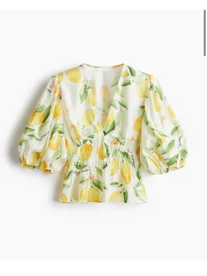 Vit blus med citronmönster och puffärm - Supersöt vit blus med citronmönster och gröna blad. Blusen har v-ringning, puffiga trekvartsärmar och smock i midjan för en snygg passform. Perfekt för dig som vill ha en fräsch och somrig look!