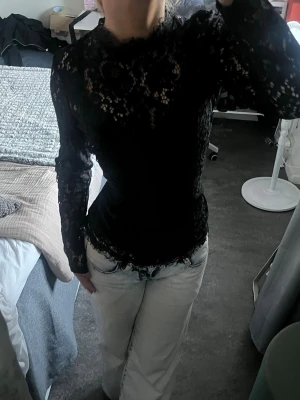 Svart spetsblus långärmad - Snygg svart spetsblus med lång ärm och hög hals. Den har ett inbyggt linne men det går lätt att klippa bort det om man vill. Den har ingen stretch men har en liten dragkedja där bak. 