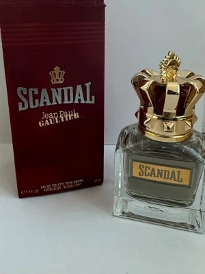 Scandal Pour Homme EdT 50ml Jean Paul Gaultier - Säljer denna eau de toilette som jag fick i present. Har använt den ett par gånger.                        Scandal Pour Homme Eau de Toilette från Jean Paul Gaultier i 50 ml flaska. Flaskan är genomskinlig med en guldig och vinröd krona som lock, och etiketten är guldig med texten SCANDAL. Förpackningen är vinröd med gulddetaljer.