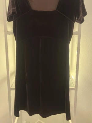 Mörkbrun sammetsklänning Hennes - Supersnygg mörkbrun sammetsklänning från Hennes Collection i kort modell. Klänningen har korta ärmar och en enkel, rak siluett som ger en vintagevibe. Perfekt för dig som gillar mjuka material och klassisk stil.