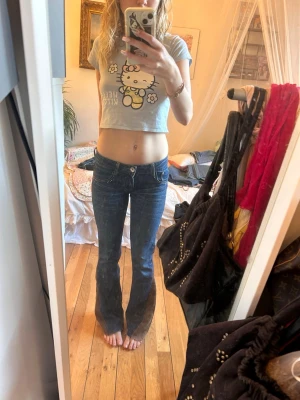Blå bootcut jeans med detaljer - Säljer ett par blå bootcut jeans med låg midja och snygga silvriga detaljer på fickorna. Jeansen har klassisk femficksdesign och är i stretchigt denimtyg som sitter tajt upptill och släpper ut vid benen. Perfekta för en trendig och avslappnad look.