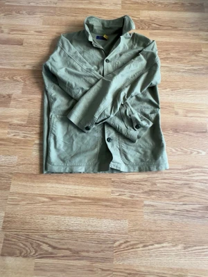 Olivgrön overshirt från Polo Ralph Lauren - Stilren olivgrön overshirt från Polo Ralph Lauren i bomull. Klassisk krage, knäppning framtill och tre stora fickor. Perfekt lager-på-lager-plagg med avslappnad passform och snygga detaljer. Enkelt att matcha med jeans eller chinos.