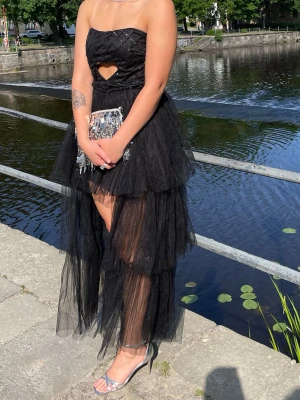 Svart Långklänning / Balklänning / Fest klänning - Säljer nu min balklänning från Lace & Beads som endast är använd en gång. Det är en axelbandslös klänning med paljetter och ett hjärtformat ’cut-out’ på överdelen. Nedtill är den kortare där fram och längre där bak, massa lager av tyll! För referens är jag 176cm lång och brukar ha storlek 38/40. Men det är en storlek 12 och Petite modell. Men den har suttit som en smäck på mig. Jag tror dock att för någon som är snäppet kortare hade denna varit perfekt! Skriv för fler bilder, mått eller frågor<3
