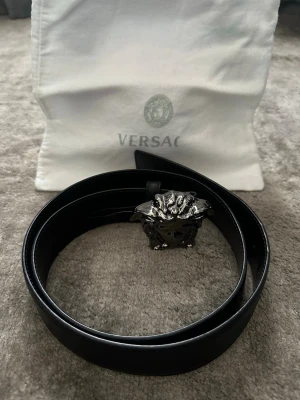 Svart skärp från Versace med Medusa-spänne - Svart bälte med ett Medusa-spänne i metall. Bältet har texten "VERSACE MADE IN ITALY" präglad på insidan. Detaljer som "DCU4140.DGOVV" och "90/36" finns också präglade på insidan av bältet. En vit tygpåse med "VERSACE"-logotypen medföljer.  Storlek : 90/36 Skick : 9/10 Nypris : 4900kr  Samtliga plagg tvättas och fixas till innan försäljning så att du får dem i bästa möjliga skick.  Har man några frågor/funderingar är det bara att höra av sig!
