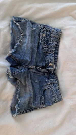 Blå jeansshorts med fransig kant - Snygga blå jeansshorts med lite slitna kanter. Vanliga fickor fram och bak. De sitter nice och är perfekta när det är varmt ute.