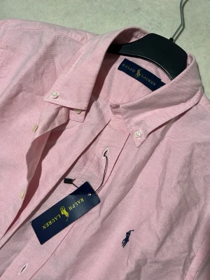 Ralph Lauren - Klassisk och stilren skjorta från Ralph Lauren i en snygg rosa färg med ikonisk broderad logga på bröstet. Perfekt för en clean och fräsch look funkar både till vardag och uppklätt.
