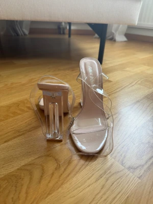 Klara klackpumps med transparent rem - Säljer ett par trendiga klackpumps från Public Desire med transparenta remmar och rund tå. Färgen är nude/beige med detaljer i plastmaterial. Perfekta för dig som gillar en modern och stilren vibe.