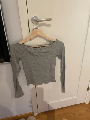 Grå långärmad croppad topp - Snygg grå långärmad topp med croppad passform och bred urringning.  Mjuk och stretchig, troligtvis i bomullsmix. Enkel och stilren design som funkar till många outfits. Egentligen storlek 158/164 men passar en xxs/xs. 