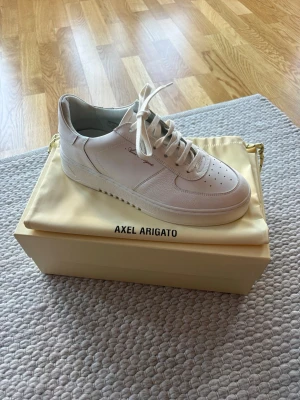 Oanvända vita sneakers från Axel Arigato orbit vintage - Helt oanvända stilrena vita sneakers från Axel Arigato i läder med diskret logga på sidan. Klassisk låg modell med perforerad tå, vita skosnören och robust sula. Perfekta för dig som gillar minimalistisk och clean stil.