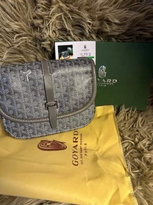Grå mönstrad väska - Snygg grå handväska med klassiskt mönster och detaljer i läder. Väskan har ett lock med spänne framtill och levereras med original dustbag och box. Perfekt för dig som gillar exklusiva accessoarer och vill sticka ut med en ikonisk design.