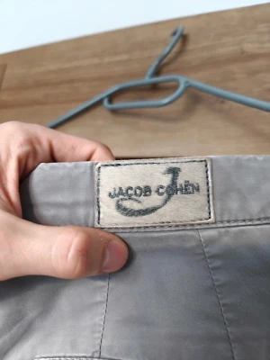 Jacob Cohën chinos - grå | Strl 48/W32 | - Snygga gråa byxor från det exklusiva italienska märket Jacob Cohën – kända för sin premium kvalitet och ikoniska detaljer! Storlek 48 / W32, i mycket bra skick utan anmärkningar. Ett givet val för dig som vill klä dig lyxigt utan att betala butikspris. Passa på – såna här fynd försvinner snabbt!
