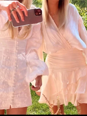 vita kort klänningar med volang från gina tricot  - Säljer den populära klänningen från gina tricot. Superfin kort omlottklänning i vit satin från gina tricot. Klänningen har långa, vida ärmar, markerad midja och volangig kjol. Snygg knytning i halsen och lätt glansigt material som ger en lyxig känsla. Perfekt för sommarens alla tillfällen! Endast använd 1 gång.💗 Storlek 34