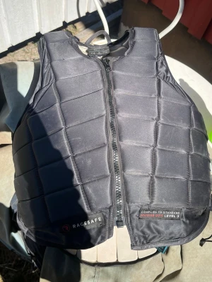 skyddsväst från Racesafe - Nypris. 3500kr, Skyddsväst från Racesafe i svart med quiltad design och dragkedja framtill. Västen är tillverkad i syntetmaterial och är speciellt framtagen för ridning. Perfekt för dig som vill ha extra skydd vid hästaktiviteter.