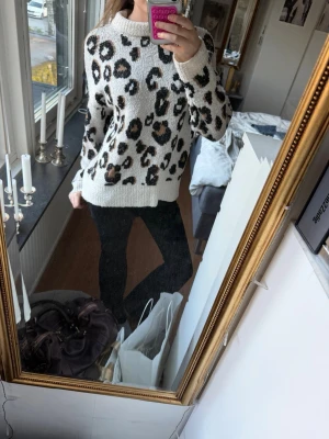 Stickad leopardmönstrad tröja🐆💞 - Säljer en stickad tröja i vitt med leopardmönster i svart och brunt. Tröjan har en rak passform, rund halsringning och långa ärmar. Jätte söt och fin, älskar mönstret och känslan! Jag viker ner kragen för tycker det är finare så men de är upp till en själv!