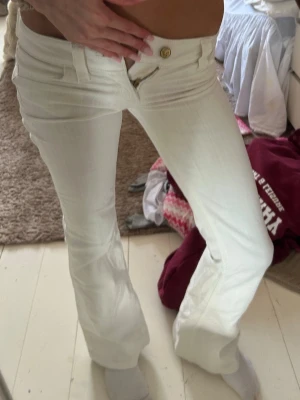  CHEAP MONDAY - Säljer ett par vita bootcut jeans från CHEAP MONDAY med låg midja och klassisk femficksdesign. Jeansen har en snygg logopatch bak och är tillverkade i denim med stretch för skön passform. Perfekta för dig som gillar retrostil och vill sticka ut. Defekter syns på bilderna