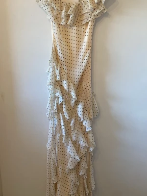 Prickig långklänning från Mango - Långklänning från Mango i ljus beige med svarta prickar. Klänningen har volangdetaljer längs sidan och upptill, samt en offshoulder-design. Tillverkad i ett lätt och luftigt material, perfekt för sommarens alla tillfällen.