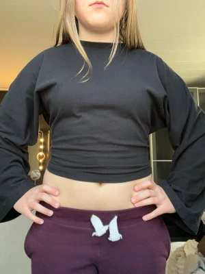 Svart croppad långärmad topp - Svart croppad topp med långa, vida ärmar och rund halsringning. Enkel och stilren design som passar perfekt till jeans eller kjol. Tillverkad i mjukt material för en bekväm känsla.