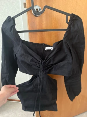 Svart topp med skurning  - Trendig svart topp från Zara med långa ärmar och snygg snörning framtill. Toppen har cut out-detaljer vid midjan och en croppad passform.