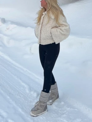Beiga Moon Boots med snörning - Säljer ett par snygga beiga Moon Boots med klassisk hög modell och snörning framtill. Skorna har en vadderad och glansig yta som håller dig varm och torr i snön. Perfekta för vinterns alla äventyr och riktigt trendiga just nu!