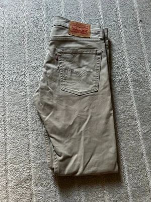 Beige jeans från Levi's - Snygga beige jeans från Levi's med klassisk femficksdesign och raka ben. Jeansen har en ikonisk läderpatch bak i midjan och den lilla röda Levi's-taggen på bakfickan. Perfekta för en clean och stilren look.