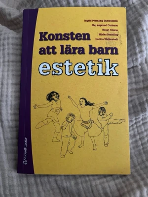 Konsten att lära barn estetik - Boken 'Konsten att lära barn estetik' handlar om barns estetiska utveckling inom musik, poesi och dans. Omslaget är gult med lila rygg och illustrationer av barn som dansar. Perfekt för dig som pluggar pedagogik eller jobbar med barn i förskola och skola.