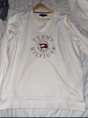 Vit sweatshirt från Tommy Hilfiger - Vit sweatshirt med rund hals och broderad Tommy Hilfiger-logga i mitten av bröstet. Tröjan har långa ärmar och klassisk passform. Perfekt för en avslappnad och stilren look.