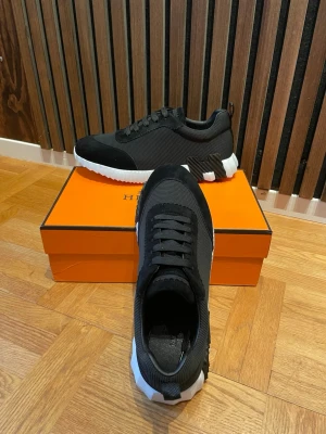 H märkes skor svart - Stilrena svarta sneakers från H med vit, räfflad sula och svarta skosnören. Ovandelen är i textil och mockaliknande material, vilket ger en modern och sportig look. Perfekta för dig som vill ha en exklusiv touch på din streetstyle.