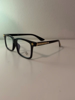 Black Chrome Hearts Bluelight Sunglasses - Säljer ett par svarta solglasögon från Chrome Hearts med rektangulära bågar och coola silverkors på sidorna och ändarna. Glasögonen har en klassisk och edgy look med tydliga metallinslag som sticker ut. Perfekt för dig som vill ha något unikt och stilrent.