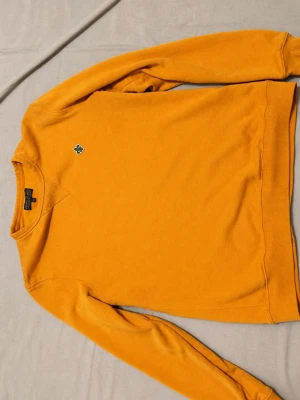 Gul sweatshirt från morris - Säljer en snygg gul sweatshirt från Morris med rund halsringning och broderad logga på bröstet. Tröjan har långa ärmar och ribbade muddar vid ärmslut och nederkant. Perfekt för dig som gillar färg och stil.