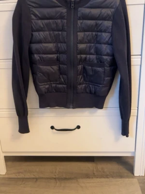 Mörkblå quiltad cardigan med dragkedja - Snygg mörkblå cardiganjacka med quiltad framsida och två fickor. Jackan har dragkedja hela vägen, ribbade muddar och är tillverkad i en mix av vadderat material och stickat tyg. Perfekt för lager på lager och en stilren look. Storlek 158/164 