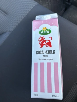 Arla rosa mjölk jordgubb 1L - En 1-liters förpackning rosa mjölkdryck från Arla med smak av jordgubb. Kartongen är vit med rosa ränder och har en illustration av en röd ko på framsidan. Perfekt för dig som gillar smaksatt mjölk och vill testa något annorlunda.