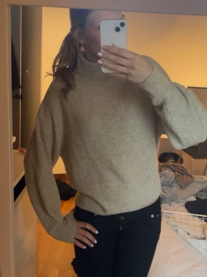 Beige stickad polotröja - Mysig beige stickad polotröja med avslappnad passform och långa ärmar. Tröjan har ribbstickad struktur och hög krage som ger en stilren look. Perfekt att matcha med jeans eller kjol för en trendig outfit.
