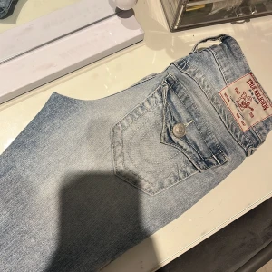 True Religion ljusblå straight jeans - Säljer ett par ljusblå jeans från True Religion med klassisk patch bak och snygga detaljerade bakfickor med lock och silverknappar. Jeansen har rak passform och är tillverkade i mjukt denimtyg. Nyligen köpta och har använts väldigt få gånger ungefär 4-6 gånger.Nytt skick.Dom är midwaist så perfekt för dig som inte vill ha så himla lågmidjade jeans men ändå inte för högmidjade.Köpta för 1299 kr på jeansbolaget.Priset kan diskuteras dessa jeans är väldigt trendiga och passar till allt
