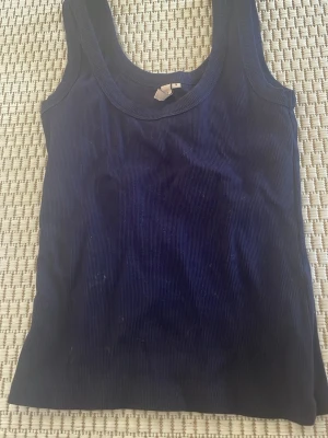 Mörkblå ribbad linnetopp från Nelly - Mörkblå ribbad linnetopp från Nelly med rund halsringning. Toppen är ärmlös och har en tight passform, perfekt att styla till jeans eller kjol. Materialet är mjukt och stretchigt för extra komfort.