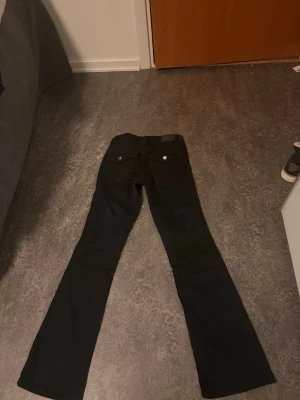 Svarta bootcut jeans med silver knappar  - Säljer ett par lågmidjade svarta bootcut jeans med snygga silverfärgade knappar och nitar. Jeansen har klassisk femficksdesign och utsvängda ben. Säljer de då de har blivit för små